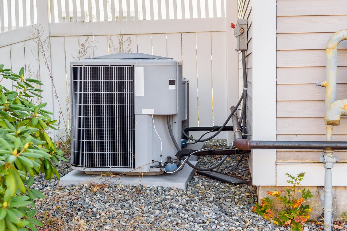 HVAC system external unit by a wooden fence in a backyard